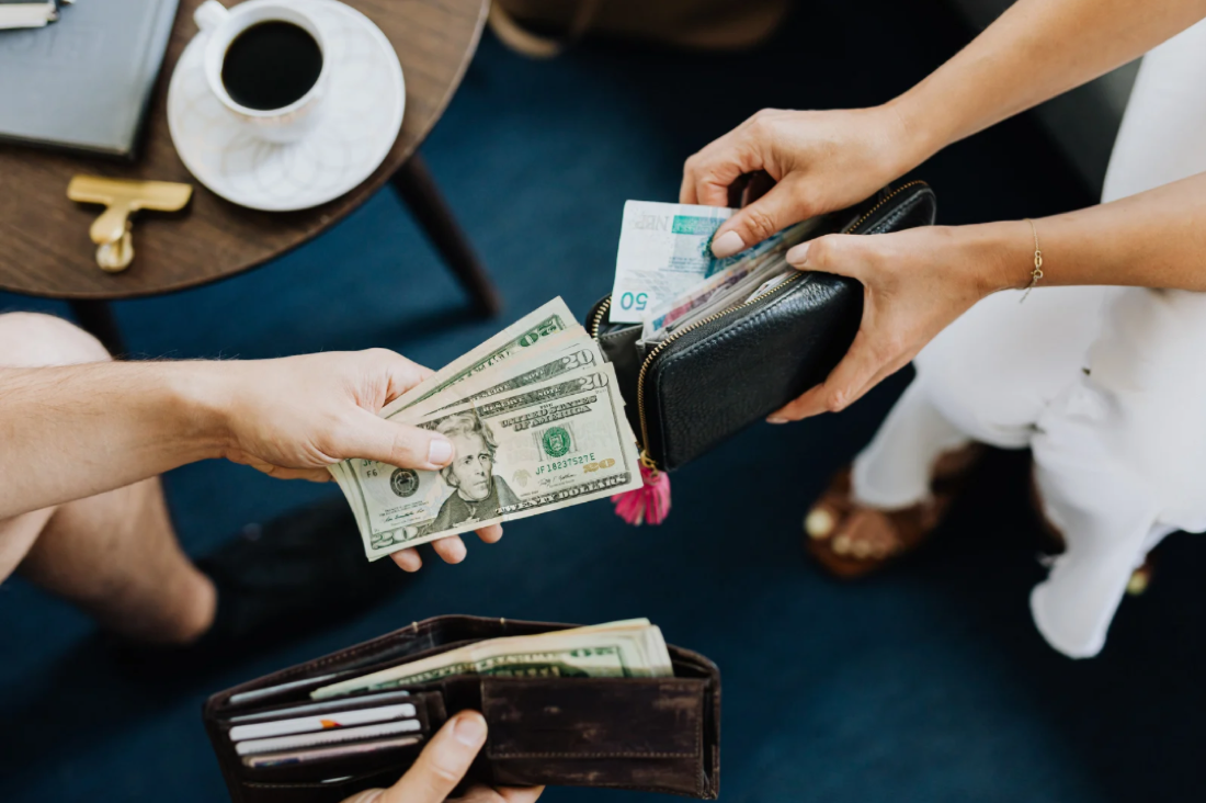 A person handing over physical cash to another, representing the shift toward secure digital payments
