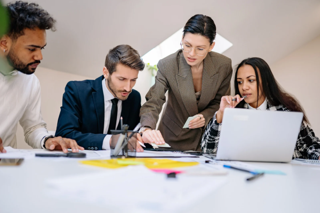 A team of colleagues collaborating around a table with a laptop and notes